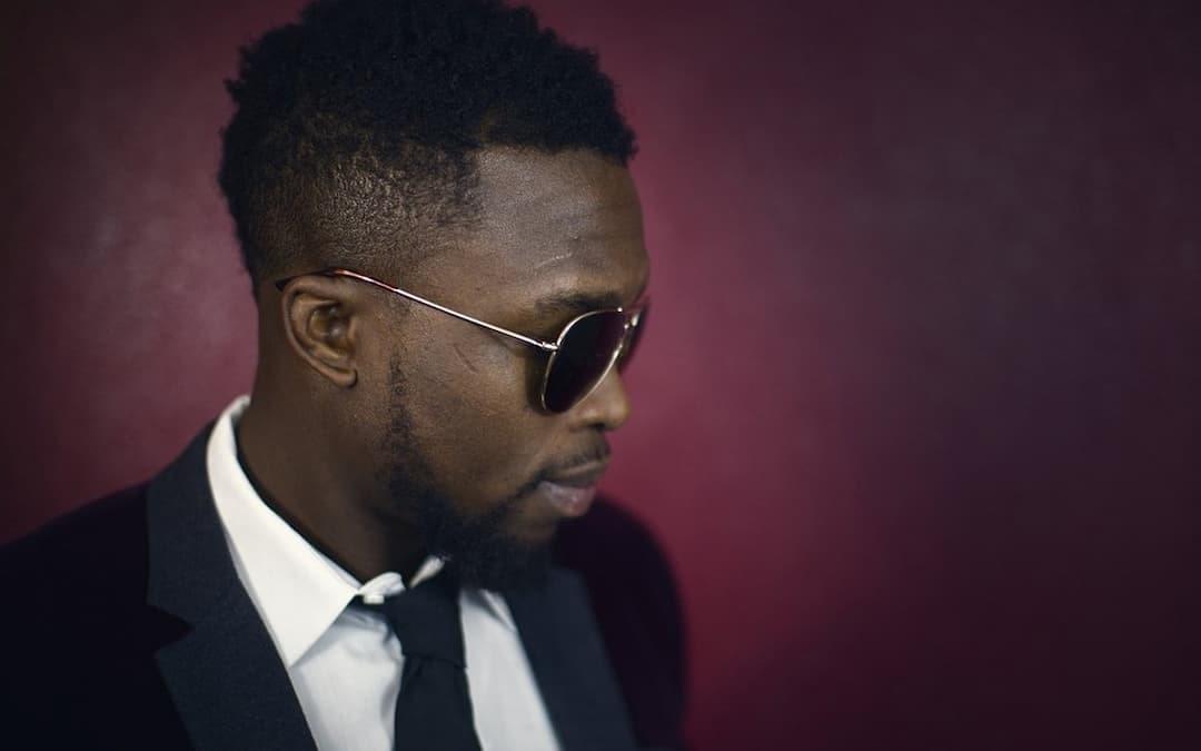 Man in a suit and tie wearing sunglasses against a red background